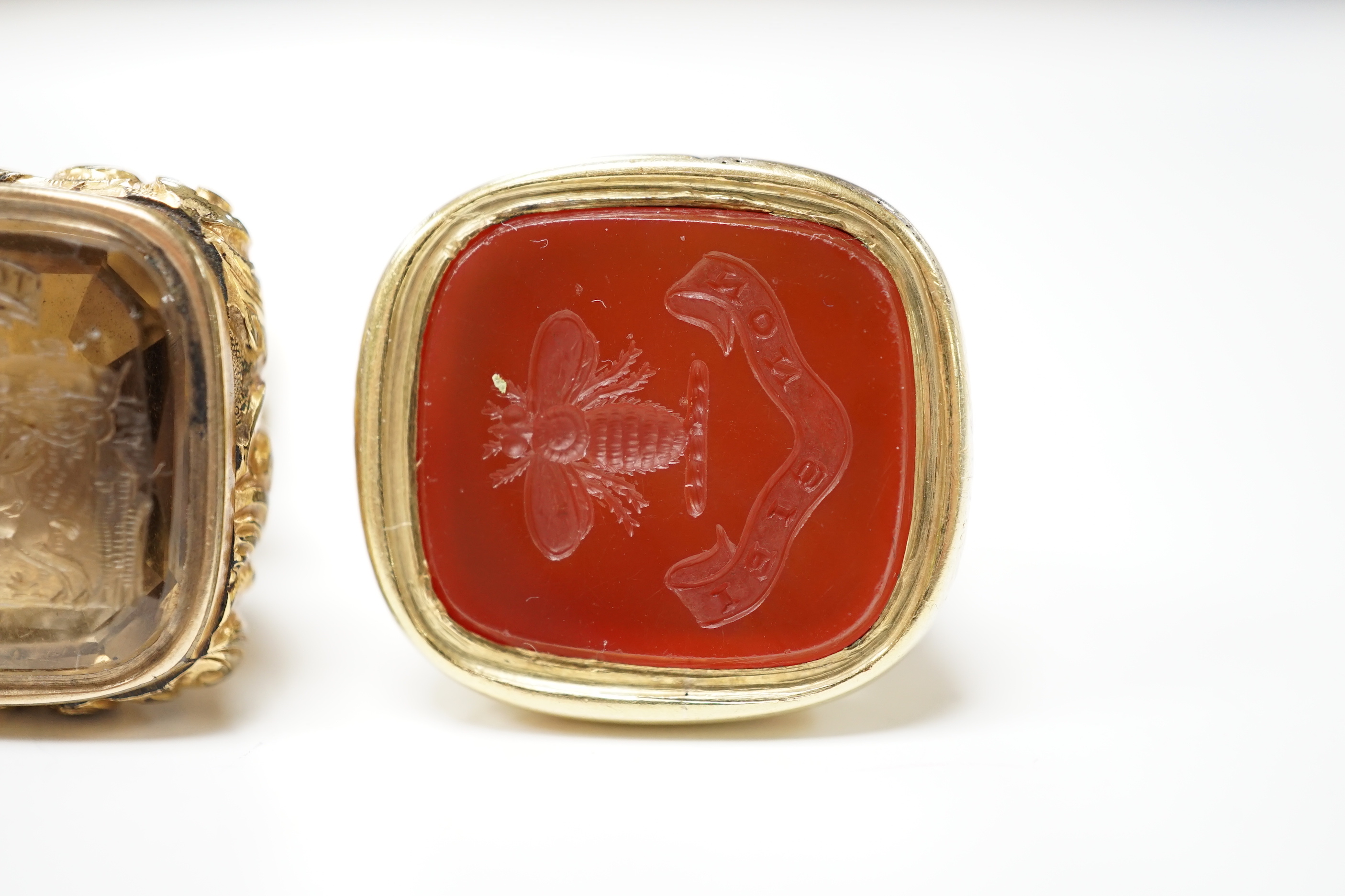 Two 19th century yellow metal overlaid fob seals, the largest 32mm with inset citrine carved with ornate crest and inscribed 'Joy of Life', the other with inset carnelian craved with bee and inscribed 'Non Sibi'.